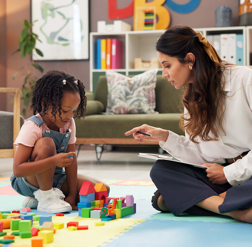 Therapist, woman and girl with clipboard, blocks and talk for evaluation, assessment or exam on floor. Person, psychologist and child with toys, advice and checklist for notes with point at clinic
